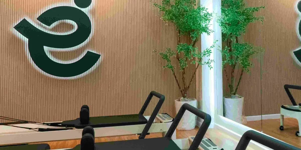Close-up of the e logo on a slatted wall above two reformers, with plants by the mirror