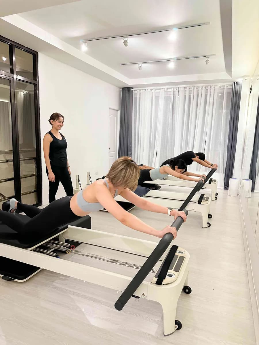 A coach watching a client do a reformer exercise in a bright white studio