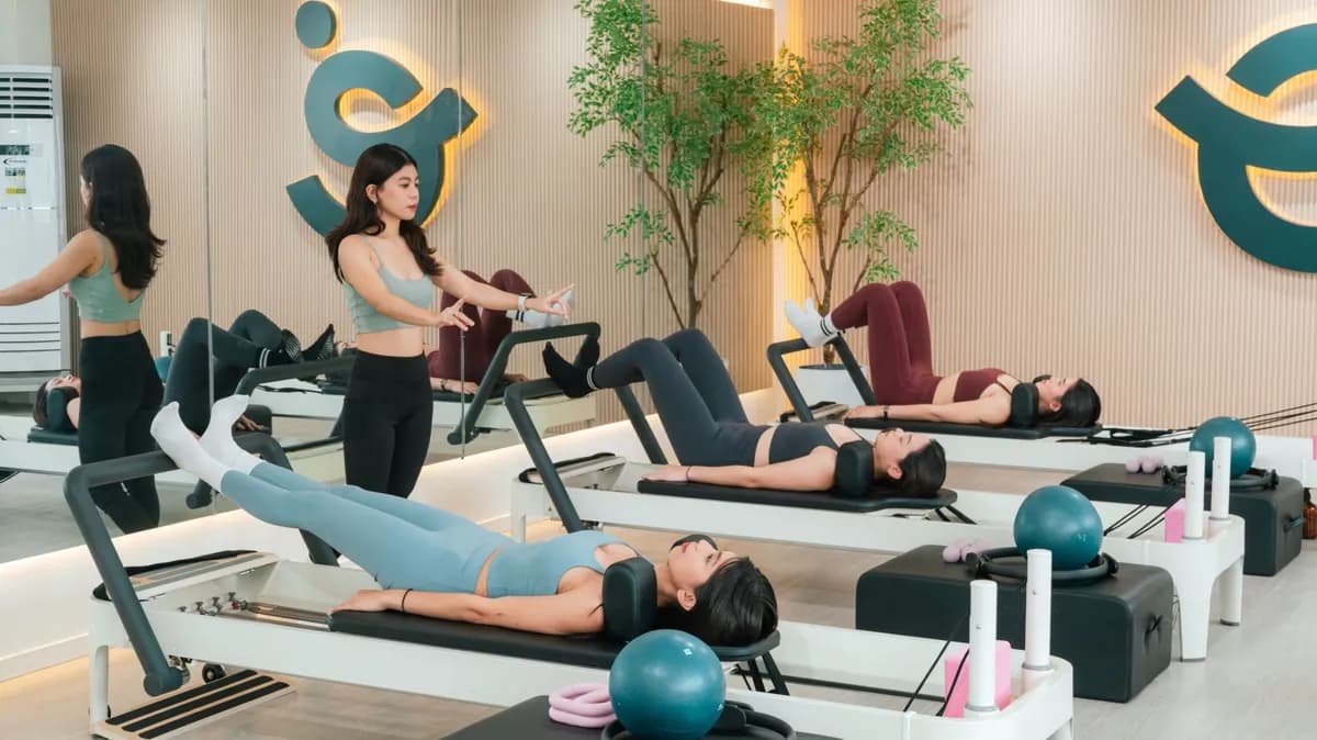 A coach leading a reformer group class, clients lying on reformers with stability balls