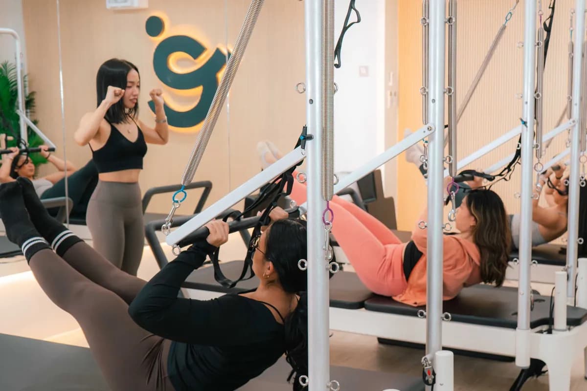 A coach between tower frames cueing a class doing roll-ups with the push-through bar
